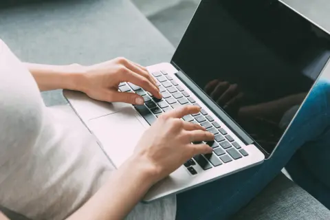 Kobieta pisze na laptopie, szukając informacji, jak zamknąć debet w Millennium.