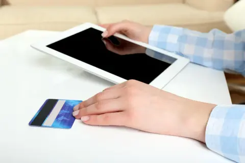 Dłonie trzymają tablet i kartę płatniczą. Zastanawiasz się, jak aktywować BLIK w Millenium?
