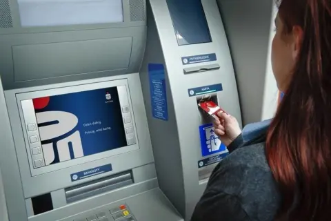 Kobieta wkłada kartę do bankomatu PKO. Ekran wyświetla logo banku i komunikat "Dzień dobry. Proszę, włóż kartę.