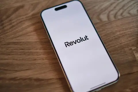 Telefon z logo Revolut na ekranie. Planujesz podróż i szukasz revolut bankomaty bez prowizji?