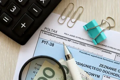 Formularz PIT-38, lupa, długopis i banknoty. Przygotowanie do rozliczenia podatku, by wiedzieć, jak wypłacić pieniądze z funduszu inwestycyjnego.