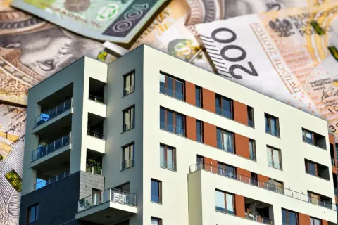 Nowoczesny budynek mieszkalny na tle polskich banknotów. Zastanawiasz się, ile obecnie wynosi oprocentowanie kredytu hipotecznego?