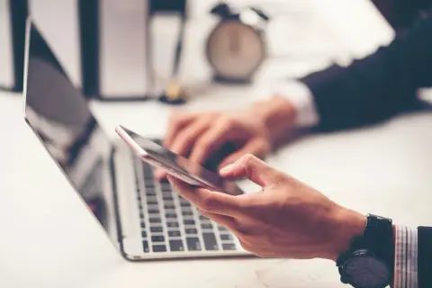 Biznesmen korzysta z telefonu i laptopa, planując przelewy Millenium.