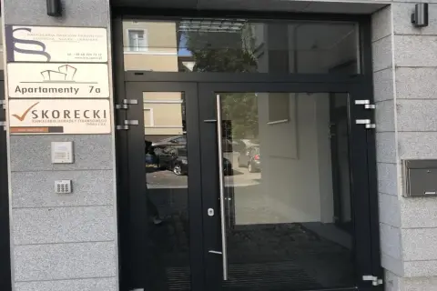 Wejście do budynku z tabliczkami: Kancelaria Radców Prawnych, Apartamenty 7a, Kancelaria Doradcy Finansowego SKORECKI.