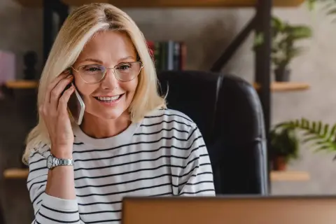 Uśmiechnięta kobieta w okularach rozmawia przez telefon, być może właśnie dowiedziała się, że czy smart pożyczka dzwoni do pracodawcy.