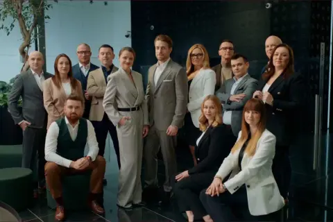 Grupa profesjonalistów w eleganckich strojach pozuje do zdjęcia w nowoczesnym wnętrzu.