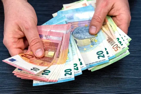 Dłonie trzymają plik banknotów euro, które są walutą w Hiszpanii. Widoczne nominały to 10, 20 i 50 euro.