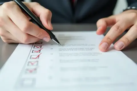 Ręka z długopisem zaznacza punkty na liście. Proces jak usunąć konto w mbank może wymagać podobnej skrupulatności.