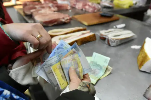 Ręce trzymają stos banknotów. Widać napisy "Національний банк України". To ukraińska waluta, hrywna, używana do zakupu mięsa na targu.