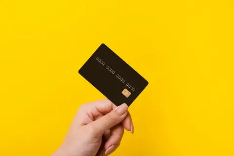 Dłoń trzyma czarną kartę z widocznym chipem i numerem. Idealna do płatności online i w sklepach.