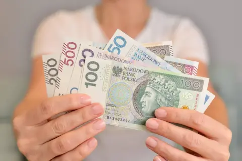 Dłonie trzymają polskie banknoty o nominałach 50, 100, 200 i 500 zł. Kto kontroluje fundusz socjalny w szkole?