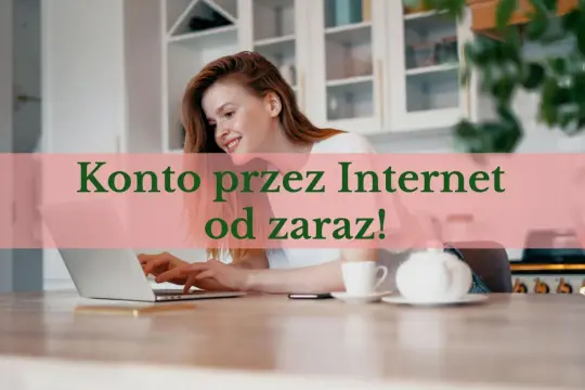 Uśmiechnięta kobieta z rudymi włosami pracuje na laptopie, zakładając konto online. Na stole stoi filiżanka i czajniczek.