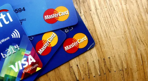 Kilka kart płatniczych, w tym Visa Platinum i karty debetowe z logo MasterCard, leżą na drewnianym blacie.