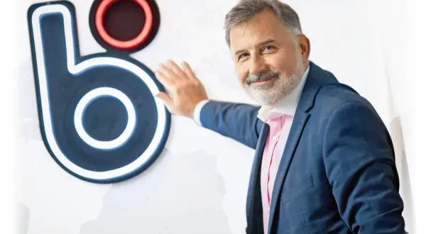 Mężczyzna w garniturze opiera się o logo, które może sugerować, kto wymyślił BLIK.