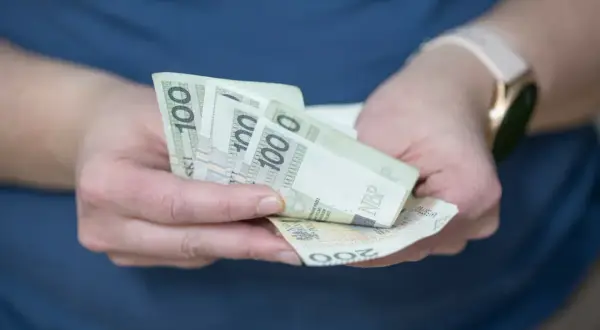 Dłonie trzymające banknoty 100 zł i 200 zł. Zastanawiasz się, o ile wzrośnie oprocentowanie lokat?