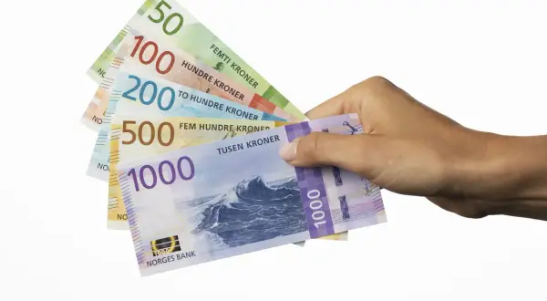 Dłoń trzyma banknoty: 50, 100, 200, 500 i 1000. To korony norweskie, czyli jaka waluta jest w Norwegii.