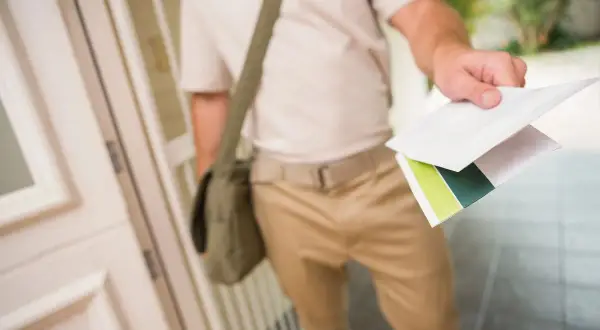Listonosz z torbą na ramieniu podaje koperty. To ważny przekaz pocztowy.