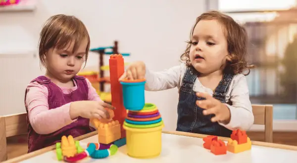 Dwie dziewczynki bawią się klockami przy stoliku. Dofinansowanie do żłobka może pomóc rodzicom w zapewnieniu opieki maluchom.