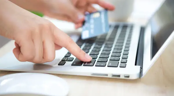 Dłoń z kartą płatniczą nad klawiaturą laptopa, przygotowuje się do wykonania przelewu. Sprawdź godziny przelewów PKO, aby zrobić to sprawnie.