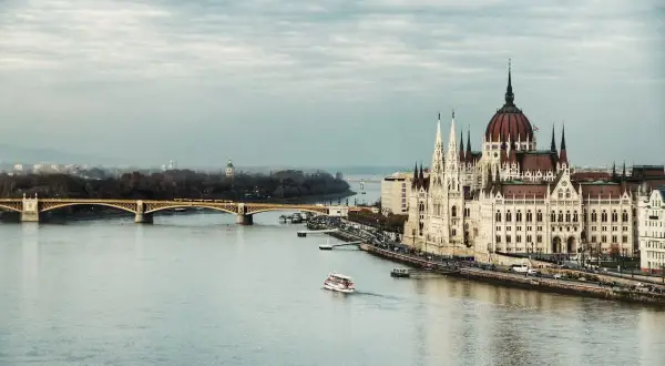 Budynek Parlamentu w Budapeszcie nad Dunajem. W tle most i panorama miasta. Pytanie: jaka jest waluta w Budapeszcie? Odpowiedź: Forint.