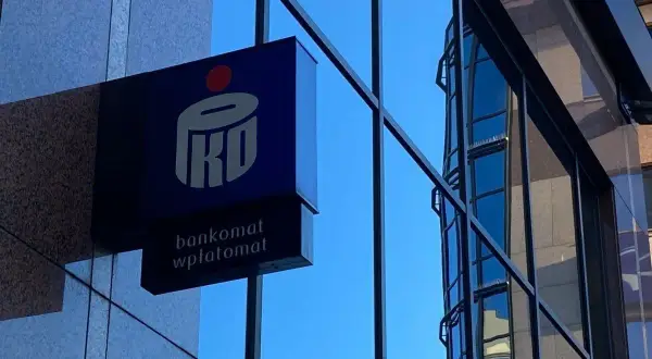 Niebieski szyld PKO BP z napisem "bankomat wpłatomat" na tle szarej ściany i błękitnego nieba. To jak eliksir dla Twoich finansów.