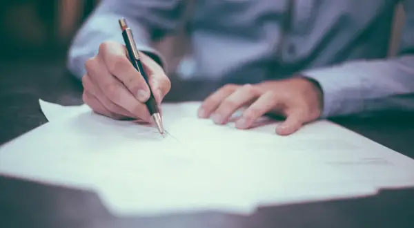 Ręka pisze długopisem na papierze. Proces sprawdzania BIK osoby zmarłej wymaga analizy dokumentów.