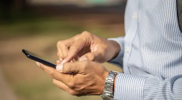 Mężczyzna w koszuli z długim rękawem i zegarkiem na nadgarstku korzysta z telefonu, szukając informacji, jak zamknąć konto Revolut.