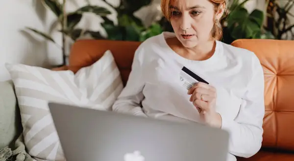 Kobieta z kartą bankową przed laptopem, szuka informacji, jak zamówić nową kartę Peako.