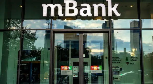 Logo mBank nad wejściem do placówki. Na drzwiach naklejki informujące o usługach, np. jak zablokować kartę mbank.