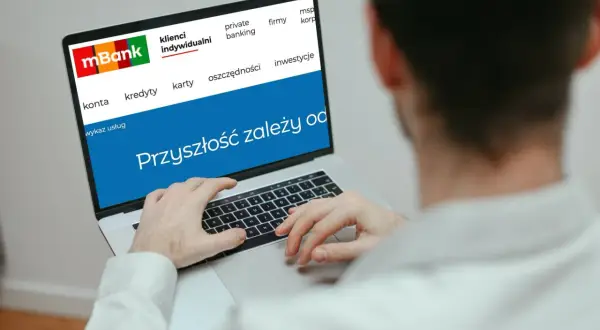 Mężczyzna korzysta z laptopa z logo mBank. Na ekranie widnieje hasło "Przyszłość zależy od..." i opcje takie jak konta, kredyty, karty, oszczędności, inwestycje. To idealne miejsce do zarządzania przelewami mBank.