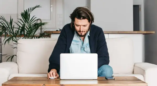 Mężczyzna siedzi na kanapie, pracując na laptopie. Wpisuje swój adres rozliczeniowy, aby dokończyć zamówienie.