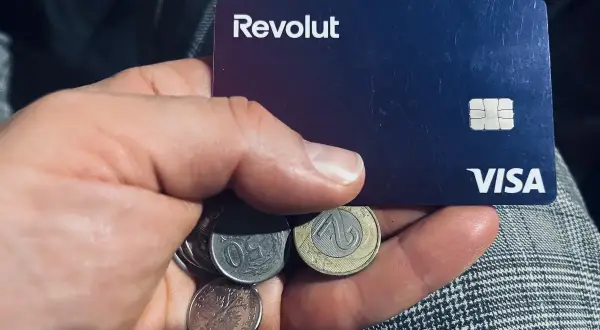 Dłoń trzyma kartę Revolut i polskie monety. Kto jest właścicielem Revolut? To pytanie, na które odpowiedź znajdziesz w aplikacji.