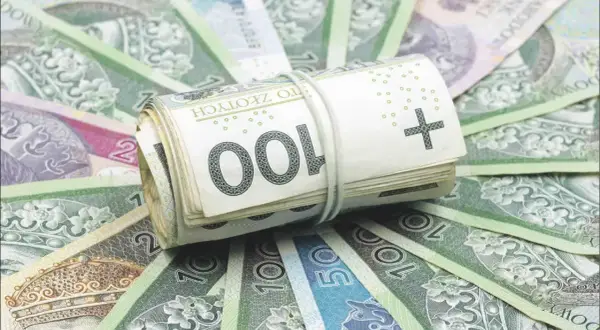 Zwijana paczka banknotów 100 zł, otoczona innymi polskimi banknotami. To symbol bezpieczeństwa finansowego, jak fundusz gwarancyjny chroniący oszczędności.
