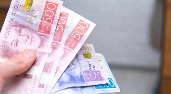 Dłoń trzyma kilka banknotów szwedzkich koron, w tym 500-koronowe.