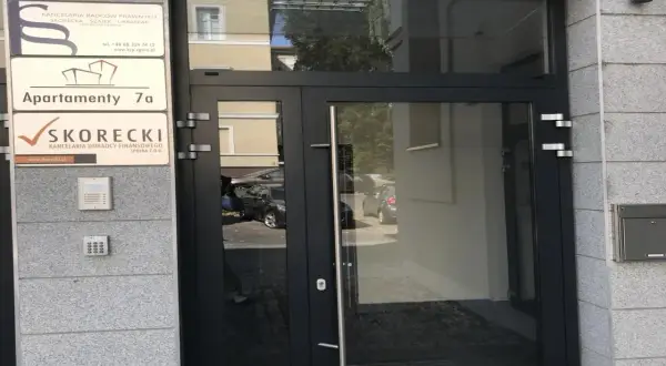 Drzwi wejściowe do budynku z tabliczkami: "Apartamenty 7a" i "SKORECKI Kancelaria Doradcy Finansowego".