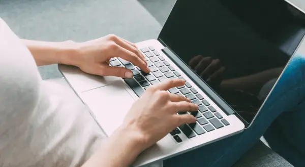 Kobieta pisze na laptopie, szukając informacji, jak zamknąć debet w Millennium.