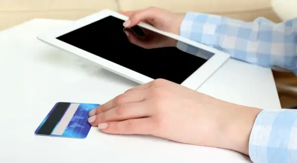 Dłonie trzymają tablet i kartę płatniczą. Zastanawiasz się, jak aktywować BLIK w Millenium?