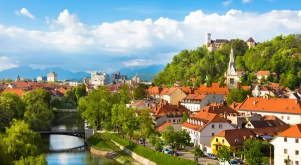 Widok na rzekę Ljubljanicę, most i miasto z zamkiem na wzgórzu w Słowenii.