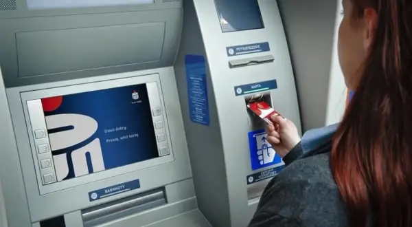 Kobieta wkłada kartę do bankomatu PKO. Ekran wyświetla logo banku i komunikat "Dzień dobry. Proszę, włóż kartę.