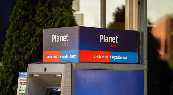 Bankomat Planet Cash z funkcją wpłatomatu, otoczony zielenią.
