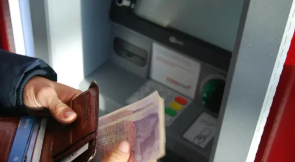 Ręka trzyma portfel z kartami i banknotami przy bankomacie. Sprawdzam saldo i dostępne środki przed wypłatą.