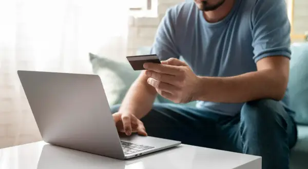 Mężczyzna z kartą kredytową przed laptopem, uczący się, jak założyć PayPal.