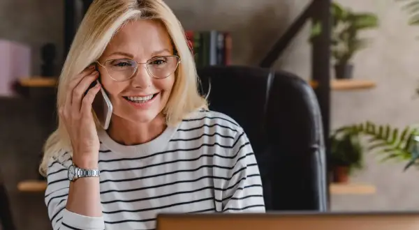 Uśmiechnięta kobieta w okularach rozmawia przez telefon, być może właśnie dowiedziała się, że czy smart pożyczka dzwoni do pracodawcy.