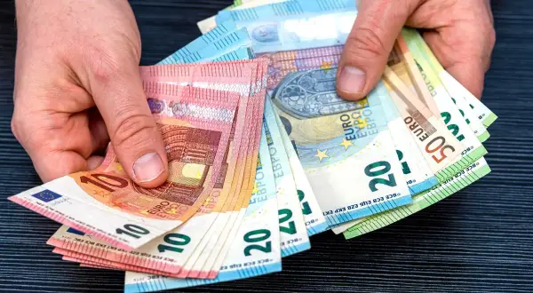 Dłonie trzymają plik banknotów euro, które są walutą w Hiszpanii. Widoczne nominały to 10, 20 i 50 euro.