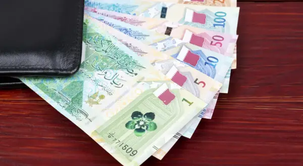 Katar jaka waluta? Na zdjęciu widać stos banknotów katarskich riali, od 1 do 200, częściowo schowanych w czarnym portfelu.