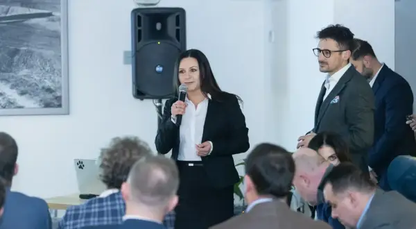Kobieta w czarnym żakiecie przemawia do publiczności, trzymając mikrofon.