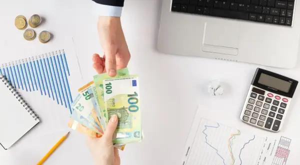 Ręce przekazują sobie euro. Obok leżą wykresy, kalkulator i monety. Zastanawiasz się, jaki podatek od pożyczki?