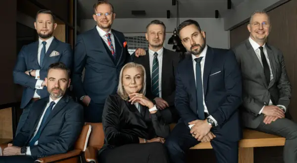 Grupa siedmiu profesjonalistów w garniturach, pozujących do zdjęcia w nowoczesnym biurze.