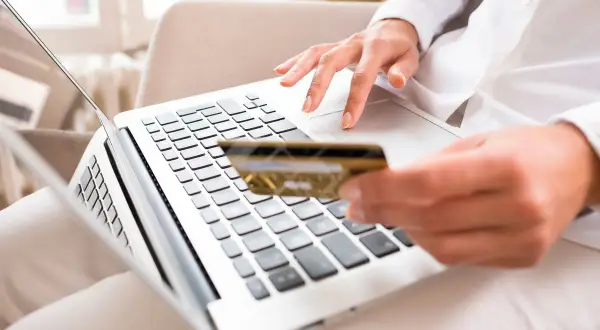 Kobieta z kartą płatniczą wpisuje kod BIC na laptopie, realizując płatność online.