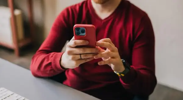 Mężczyzna w czerwonym swetrze korzysta z telefonu, szukając informacji, jak zrobić przelew ekspresowy mBank.